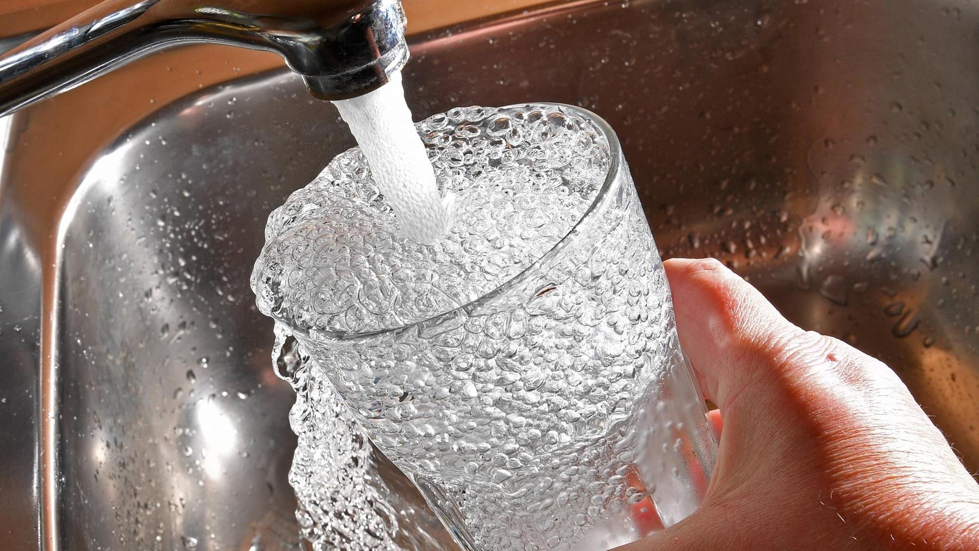 Aufsicht auf ein Glas, in das sprudelnd Wasser eingelassen wird, sodass es bereits ins Becken überläuft. Aufsicht auf ein Glas, in das sprudelnd Wasser eingelassen wird, sodass es bereits ins Becken überläuft.