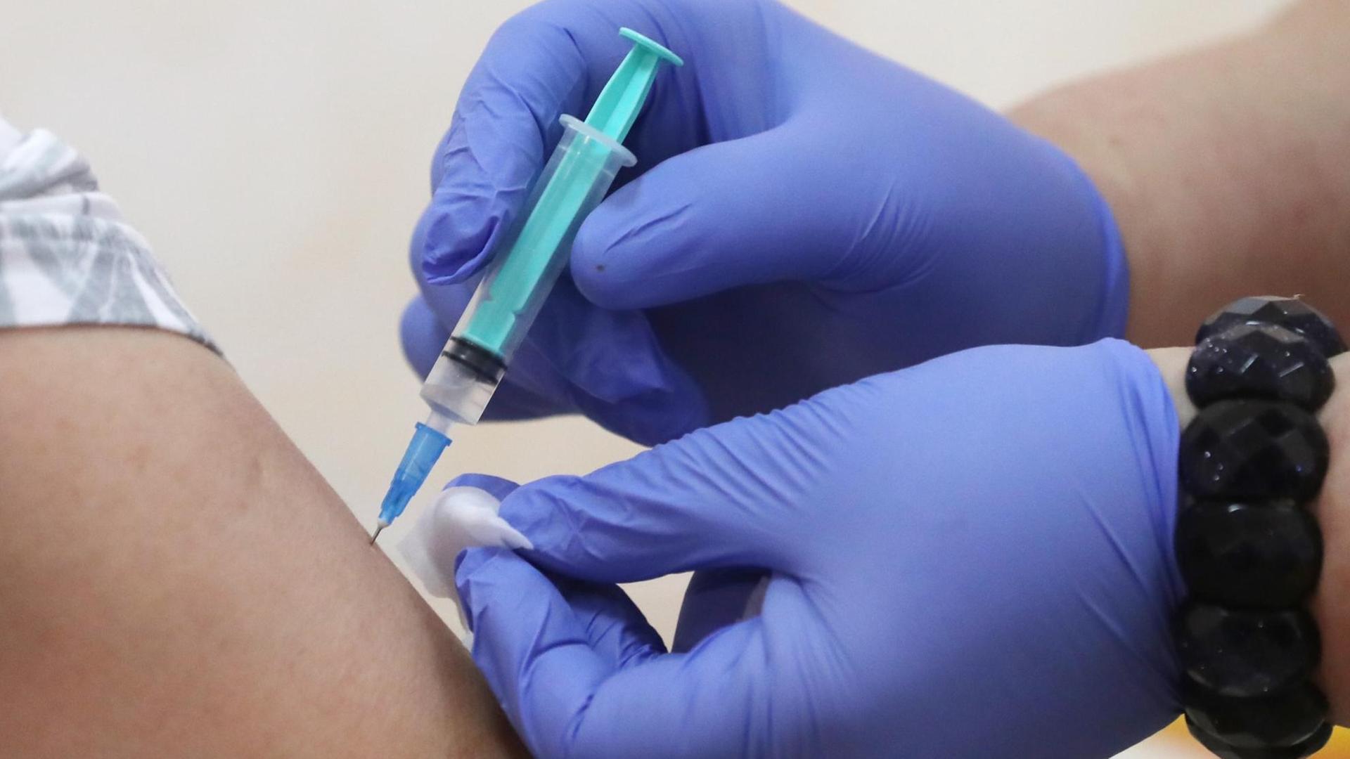 Impfung: Hände in blauen Schutzhandschuhen halten eine Spritze und einen Tupfer Impfung: Hände in blauen Schutzhandschuhen halten eine Spritze und einen Tupfer
