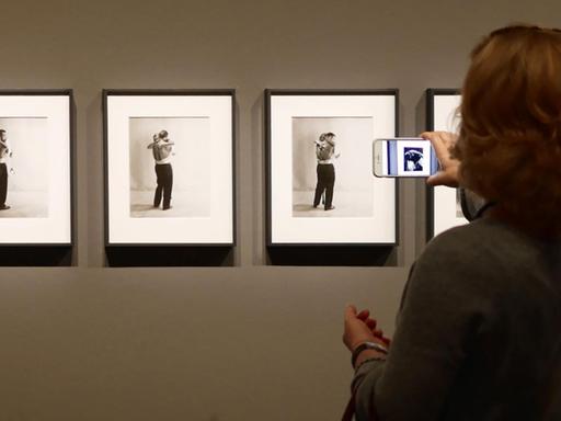 Eine Frau steht in einem Museum vor einem Bild und hält ein Handy davor.