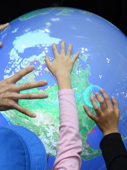 Japanische Schulkinder berühren bei einer Messe einen elektronischen Globus, der die Erhöhung des Meerwasserspiegels durch die Erderwärmung verdeutlicht.