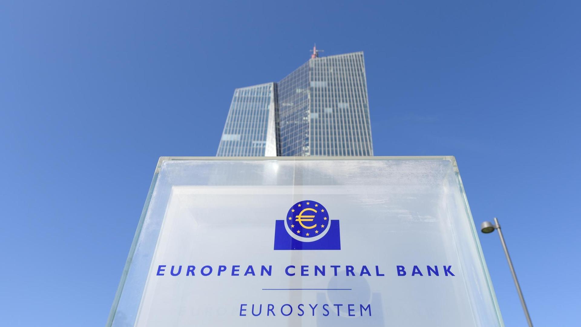 Die Zentrale der Europäischen Zentralbank (EZB) in Frankfurt am Main (Hessen) ragt hinter einer Stele mit dem EZB-Logo hoch.