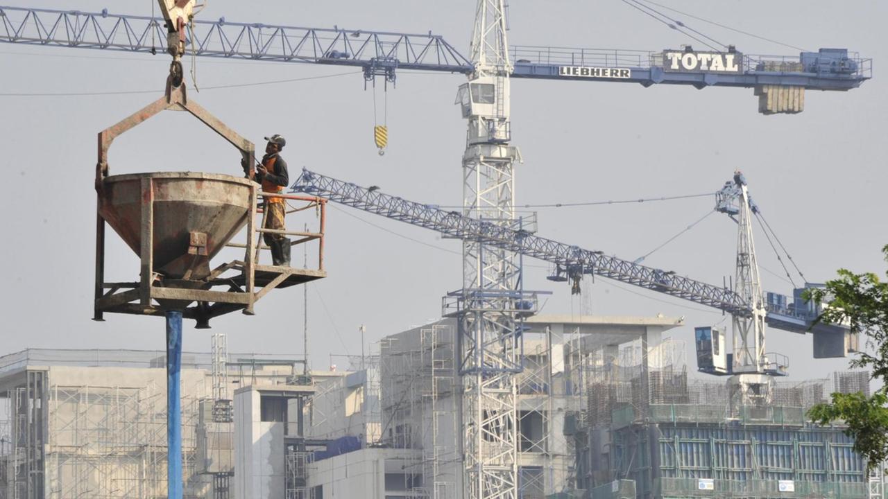 In der Luft hängend bereitet sich ein Arbeiter darauf vor, auf einer Baustelle für ein Bürohochhaus in Jakarta Zement zu gießen. In der Luft hängend bereitet sich ein Arbeiter darauf vor, auf einer Baustelle für ein Bürohochhaus in Jakarta Zement zu gießen.