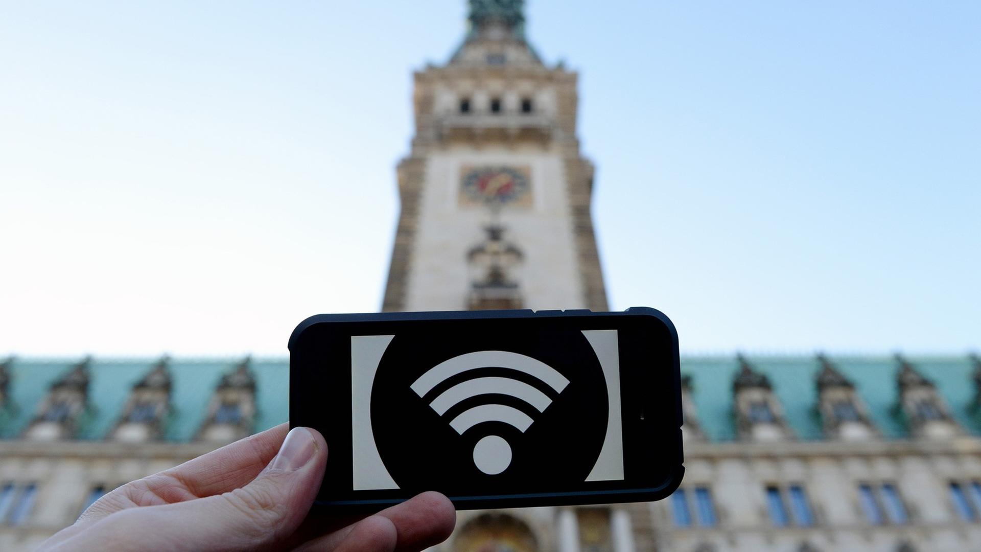 Eine Hand hält ein Schild mit einem WLAN-Symbol, im Hintergrund das Hamburger Rathaus. Eine Hand hält ein Schild mit einem WLAN-Symbol, im Hintergrund das Hamburger Rathaus.