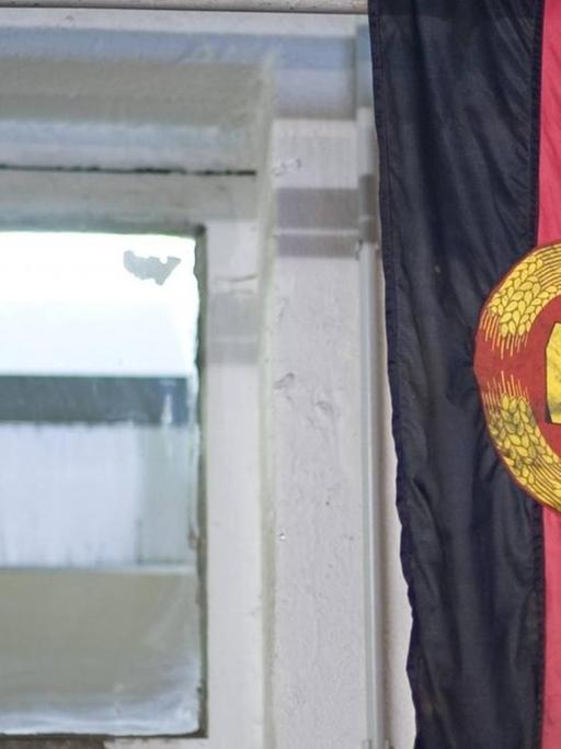 Eine DDR-Fahne mit den Symbolen Hammer und Zirkel hängt in einem Raum mit Fenster.