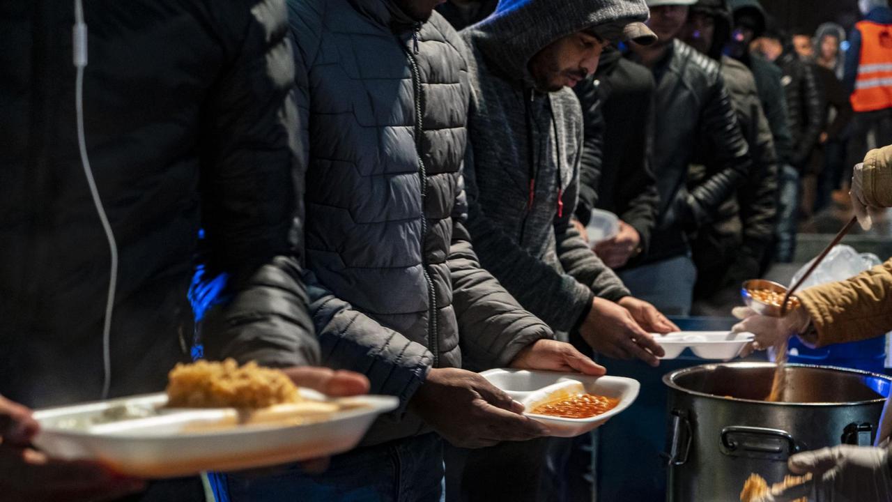 Man sieht nur die Hände von Personen, die Plastikschüsseln mit etwas zu Essen halten. Sie stehen in einer Schlange. Man sieht nur die Hände von Personen, die Plastikschüsseln mit etwas zu Essen halten. Sie stehen in einer Schlange.