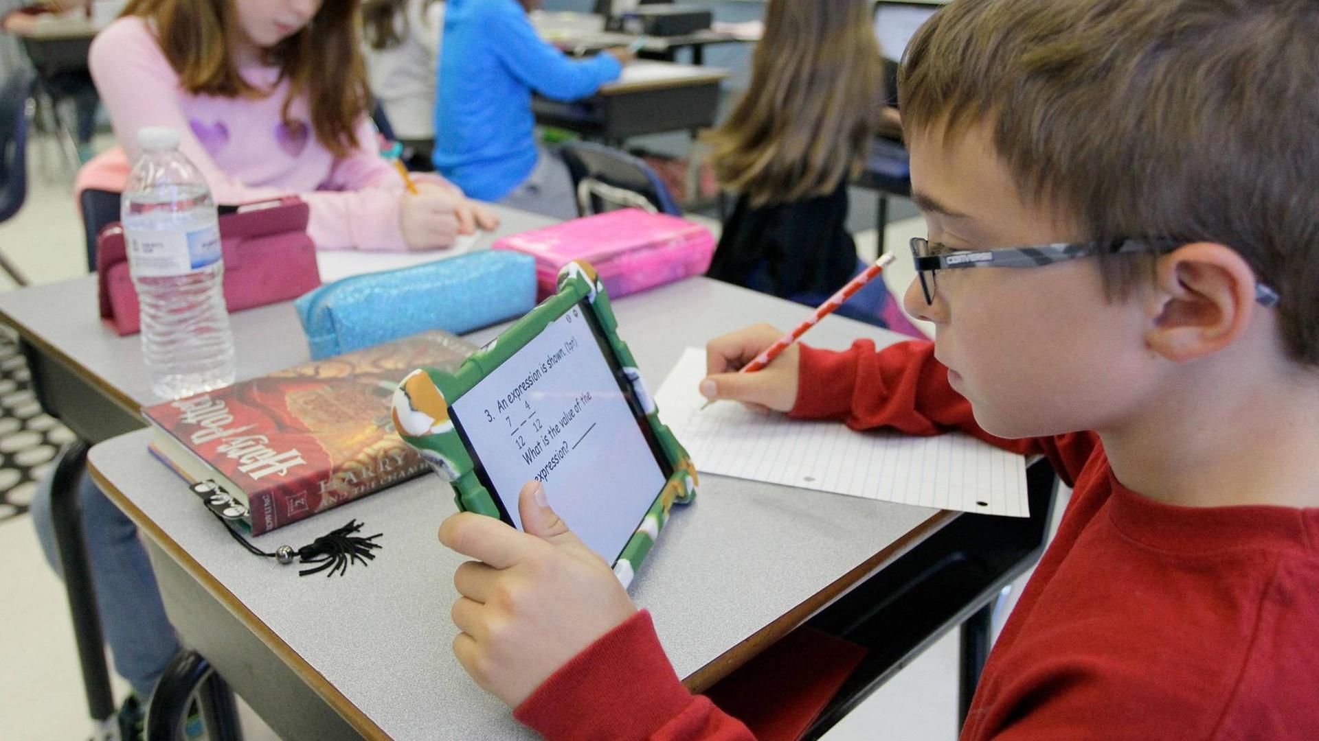 Ein Junge sitzt in einem Klassenraum und arbeitet mit einem Tablet. Ein Junge sitzt in einem Klassenraum und arbeitet mit einem Tablet.