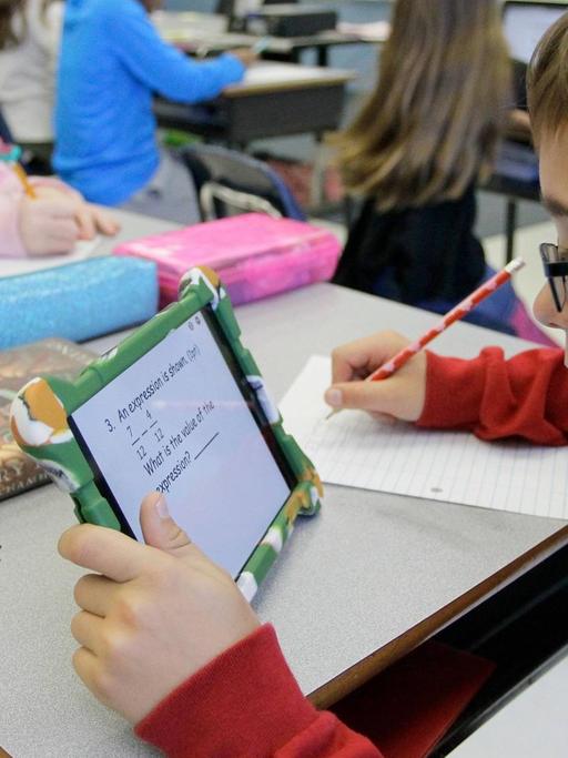Ein Junge sitzt in einem Klassenraum und arbeitet mit einem Tablet.