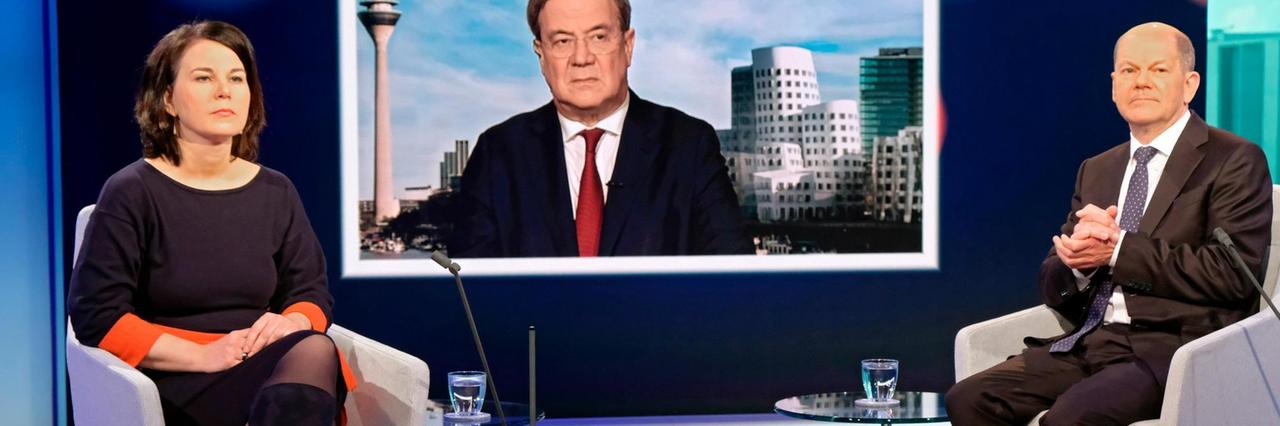 Kanzlerkandidat Armin Laschet wird auf einem Fernsehschirm gezeigt. Annalena Baerbock und Olaf Scholz sitzen im Fernseh-Studio. Kanzlerkandidat Armin Laschet wird auf einem Fernsehschirm gezeigt. Annalena Baerbock und Olaf Scholz sitzen im Fernseh-Studio.