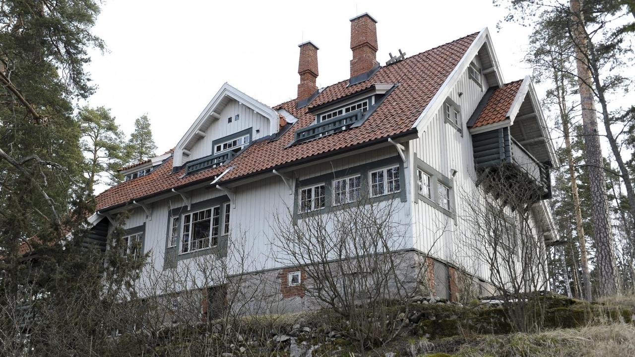 Eine großzügige Villa aus Holz mit großen Fenstern auf einem Hügel, der bewaldet ist.