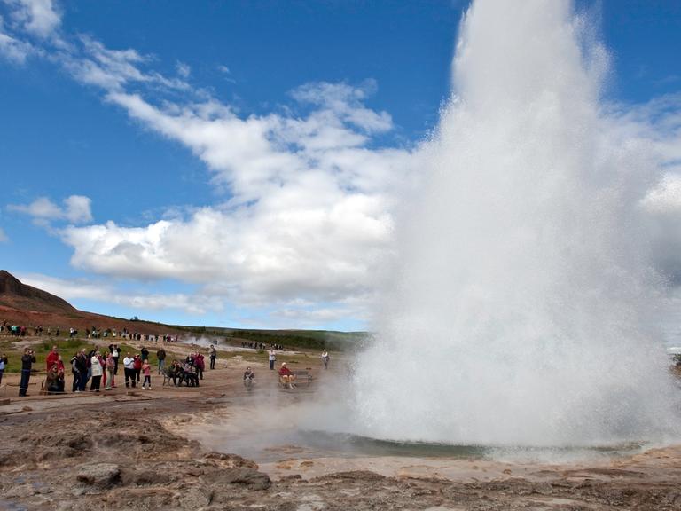 Touristen bestaunen den Geysir Strokkur auf Island.