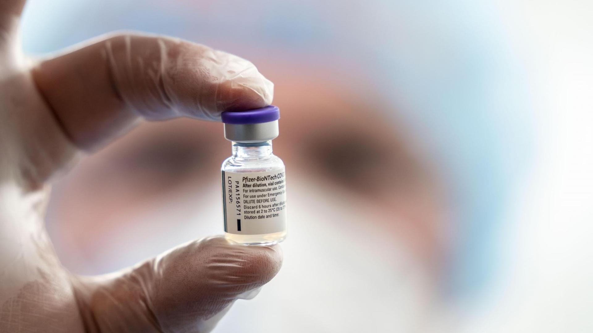 Zwei behandschuhte Finger halten eine kleine Ampulle mit dem Impfstoff von Biontech/Pfizer in der Luft Zwei behandschuhte Finger halten eine kleine Ampulle mit dem Impfstoff von Biontech/Pfizer in der Luft
