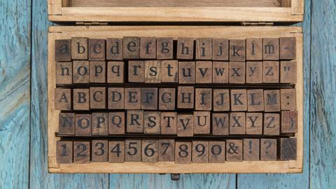 Holzstempel mit Buchstaben, Zahlen und Zeichen liegen sortiert in einer Schachtel aus Holz.