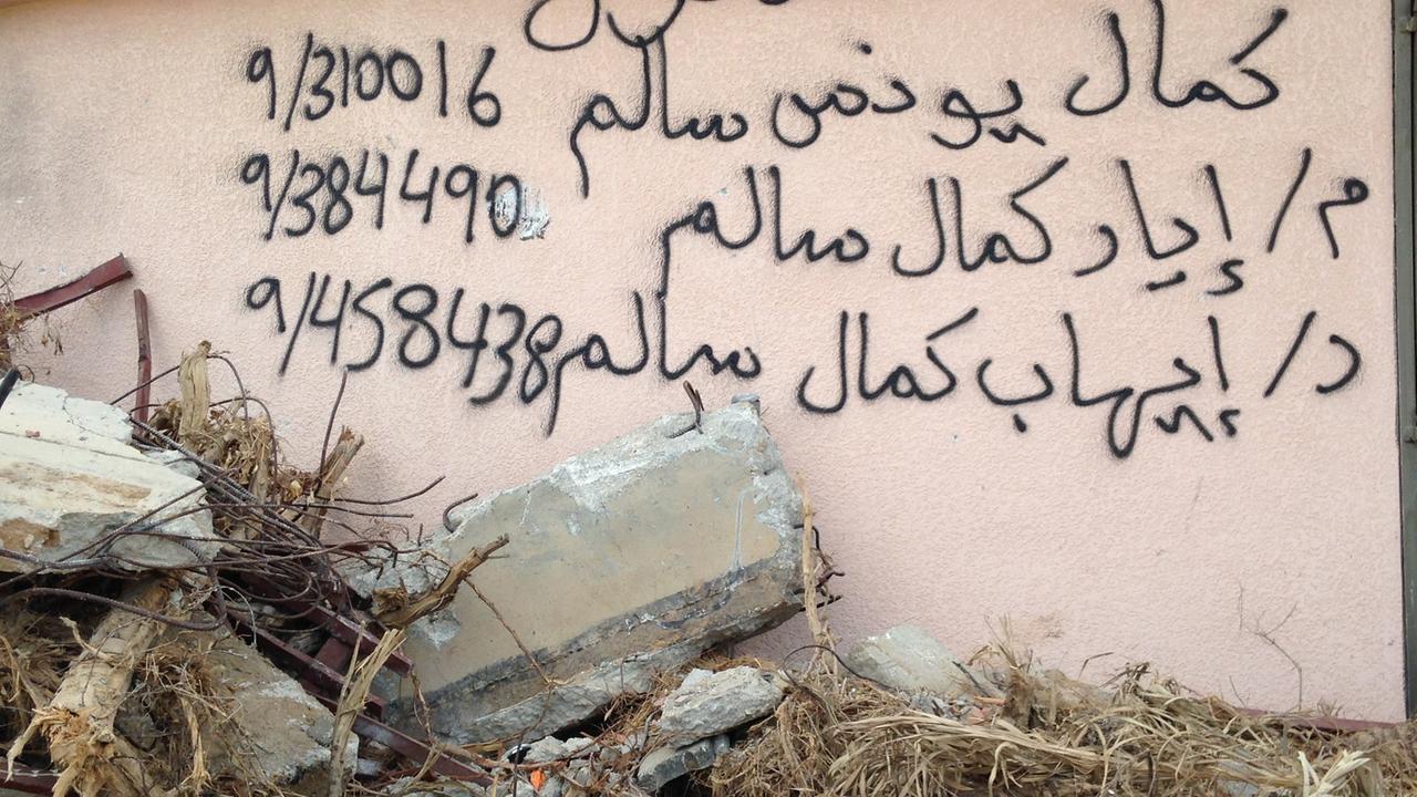 Arabische Schriftzeichen und Zahlen stehen auf auf einer Hauswand, davor liegen Steine und Trümmer Arabische Schriftzeichen und Zahlen stehen auf auf einer Hauswand, davor liegen Steine und Trümmer
