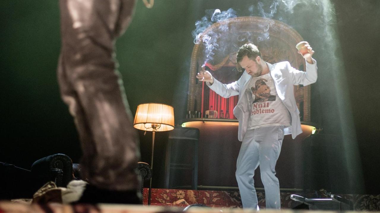 Der Schauspieler Nico Holonics hat in der einen Hand einen Bierbecher, in der anderen einen rauchenden Joint, Auf seinem T-Shirt steht "Null Probleomo". Der Schauspieler Nico Holonics hat in der einen Hand einen Bierbecher, in der anderen einen rauchenden Joint, Auf seinem T-Shirt steht "Null Probleomo".