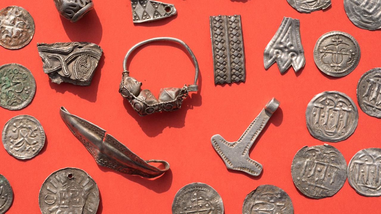 Teile des Silberschatzes von Schaprode mit Silberperlen mit Granulationsauflage, zerhacktem Silberschmuck, Thorshammeramulett und dänischen sowie ottonischen Münzen liegt auf einem Tisch. In einem Acker auf der Ostseeinsel Rügen sind Archäologen auf einen wertvollen skandinavisch dominierten Silberschatz aus dem späten 10. Jahrhundert und damit aus der Umbruchsepoche von der Wikingerzeit zum Christentum gestoßen. Teile des Silberschatzes von Schaprode mit Silberperlen mit Granulationsauflage, zerhacktem Silberschmuck, Thorshammeramulett und dänischen sowie ottonischen Münzen liegt auf einem Tisch. In einem Acker auf der Ostseeinsel Rügen sind Archäologen auf einen wertvollen skandinavisch dominierten Silberschatz aus dem späten 10. Jahrhundert und damit aus der Umbruchsepoche von der Wikingerzeit zum Christentum gestoßen.