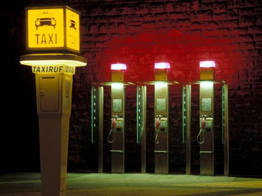 Eine Taxirufsäule und drei Telefonzellen bei Nacht.