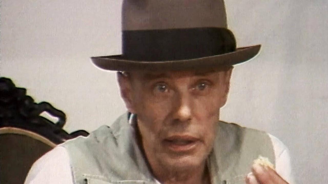 Farbfoto zeigt den Künstler Josef Reuss mit Filzhut, beigefarbener Weste, zwischen Daumen und Zeigefinger hält er eine kleine Menge Fett hoch Farbfoto zeigt den Künstler Josef Reuss mit Filzhut, beigefarbener Weste, zwischen Daumen und Zeigefinger hält er eine kleine Menge Fett hoch