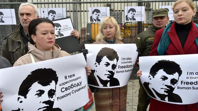 Frauen und Männer stehen vor dem Zaun der Botschaft und halten Plakate mit dem Kopf Sushchenkos und Schriftzügen in Englisch und Kyrilisch in den Händen, auf denen die Freilassung des Journalisten gefordert wird.