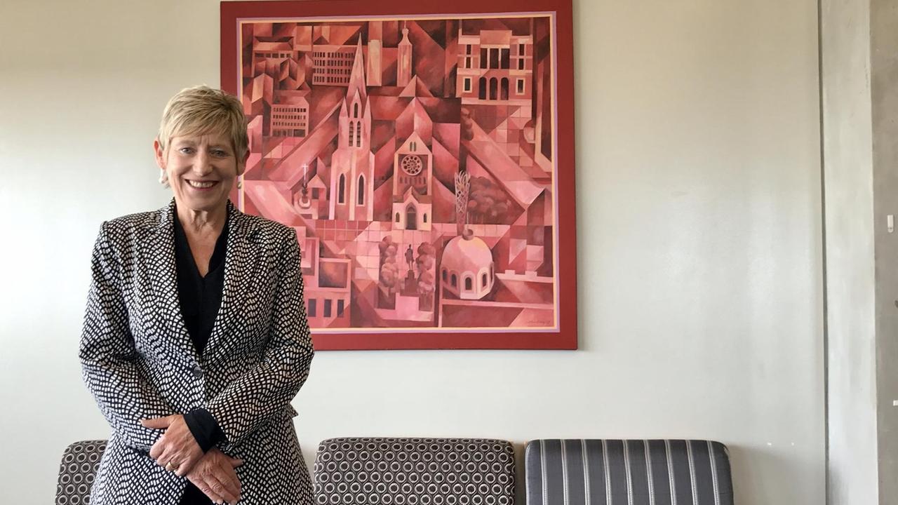 Eine Dame ganz in schwarz mit schwarz-weiß gepunktetem Jacket steht im Büro vor gemusterten Sesseln und einem Wandbild in rot. Eine Dame ganz in schwarz mit schwarz-weiß gepunktetem Jacket steht im Büro vor gemusterten Sesseln und einem Wandbild in rot.