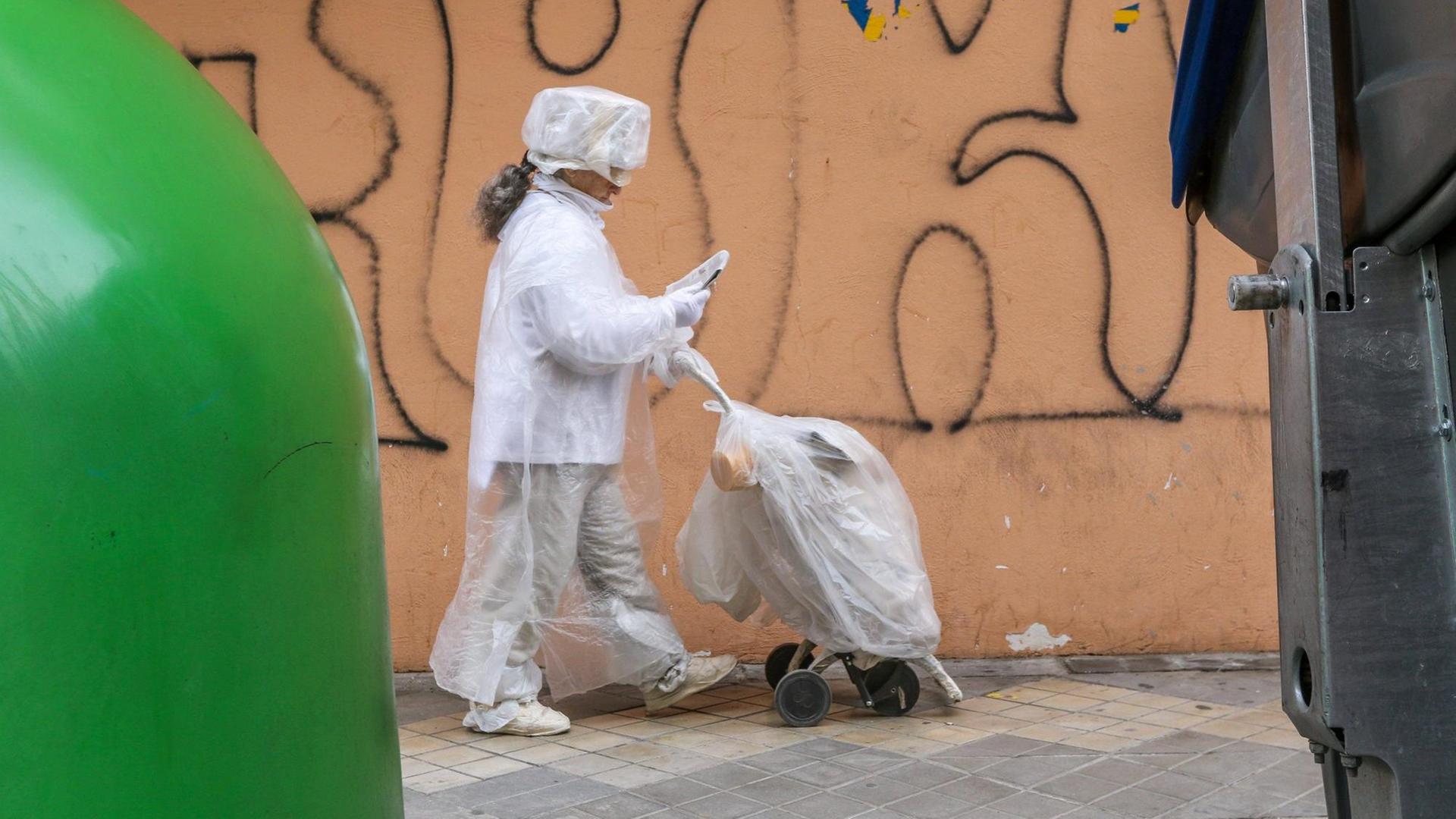 Eine in Plastikfolie gehüllte Frau geht an einer Mülltonne vorbei. Eine in Plastikfolie gehüllte Frau geht an einer Mülltonne vorbei.