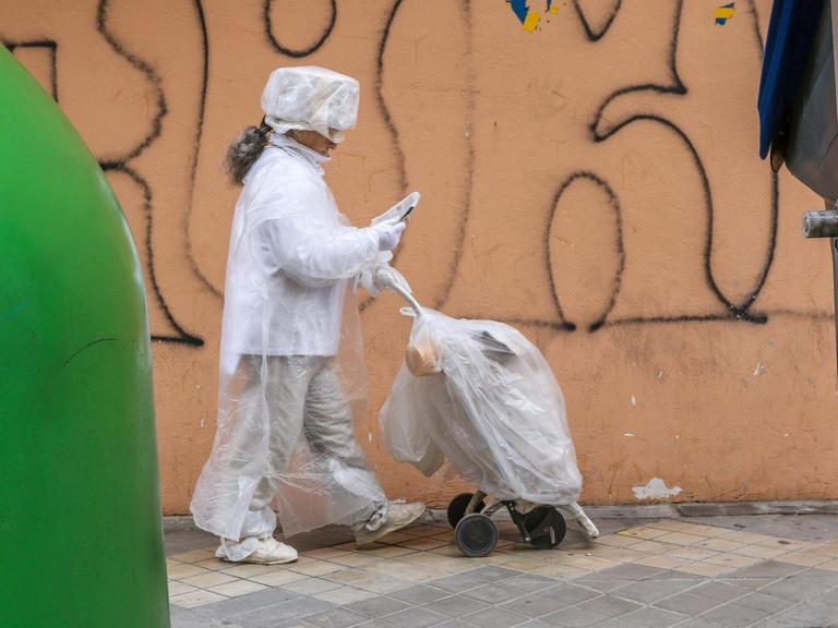 Eine in Plastikfolie gehüllte Frau geht an einer Mülltonne vorbei.