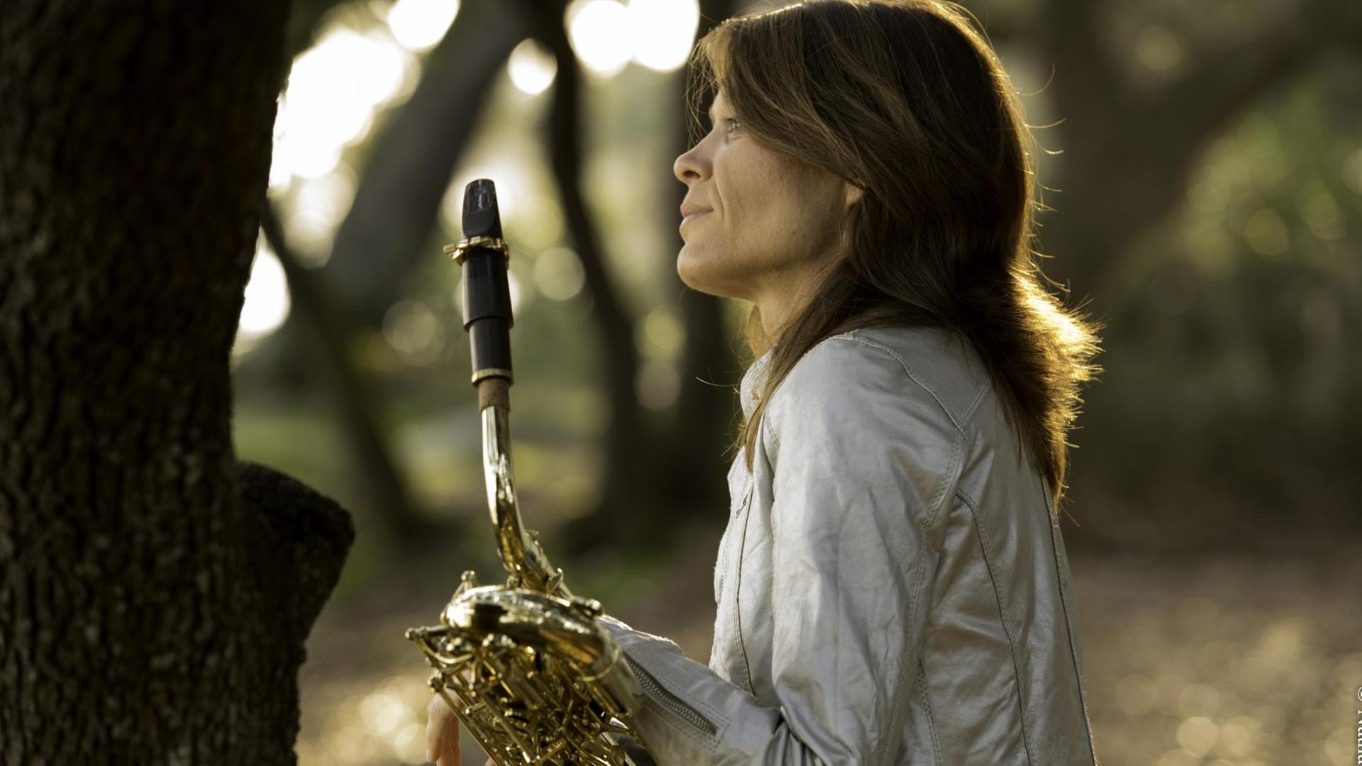 Die französische Musikerin und Komponistin Céline Bonacina steht mit ihrem Saxofon in einem Wald