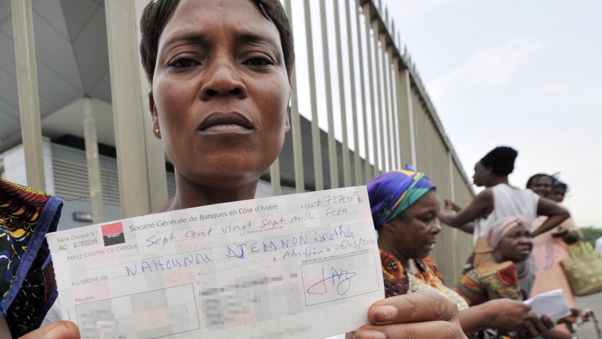 Eine Frau aus der Elfenbeinküste hält einen Scheck hoch, mit dem sie für Gesundheitsschäden durch die illegale Abladung von Giftmüll in Abidjan entschädigt wird.