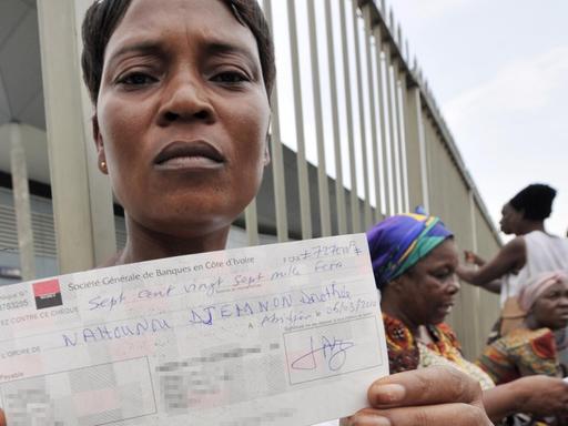 Eine Frau aus der Elfenbeinküste hält einen Scheck hoch, mit dem sie für Gesundheitsschäden durch die illegale Abladung von Giftmüll in Abidjan entschädigt wird.
