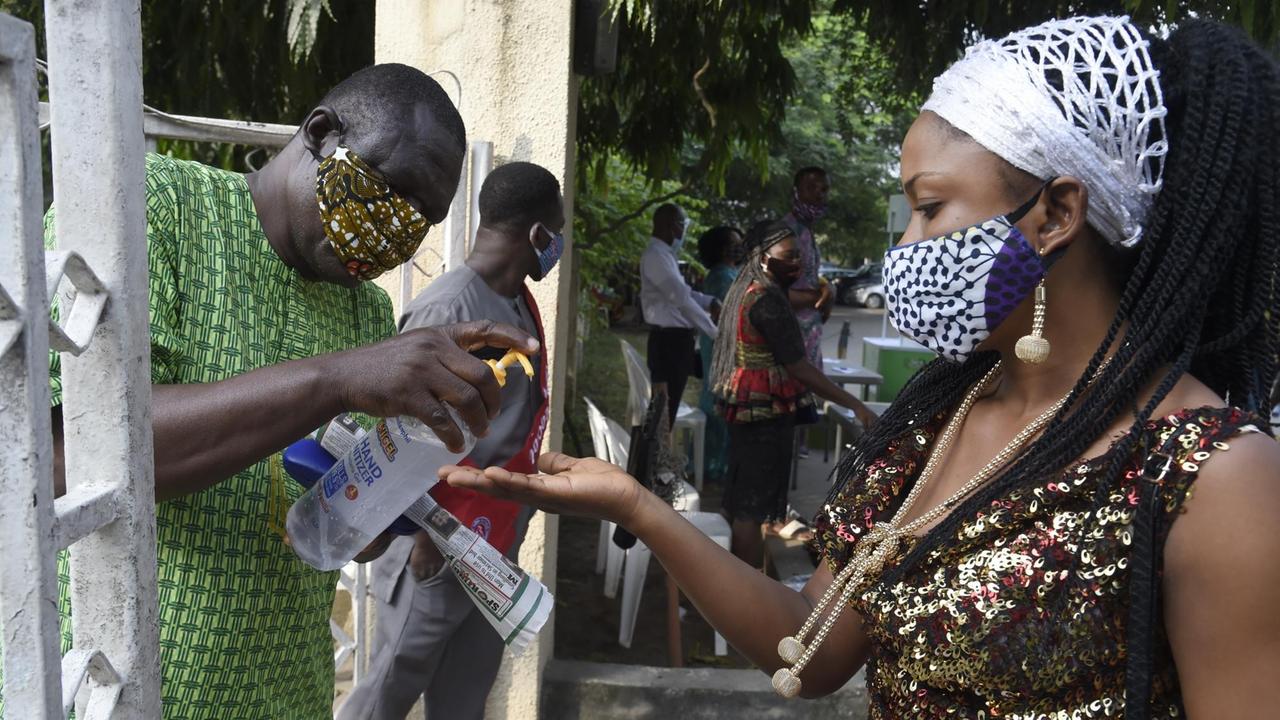 Eine schwarze Frau mit Maske desinfiziert sich in Nigeria vor dem Kirchenbesuch die Hände. Eine schwarze Frau mit Maske desinfiziert sich in Nigeria vor dem Kirchenbesuch die Hände.