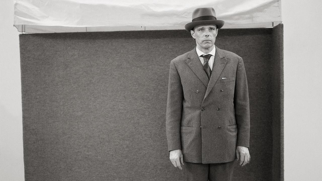 Joseph Beuys steht mit Hut und Anzug vor einer Skulptur. Joseph Beuys steht mit Hut und Anzug vor einer Skulptur.