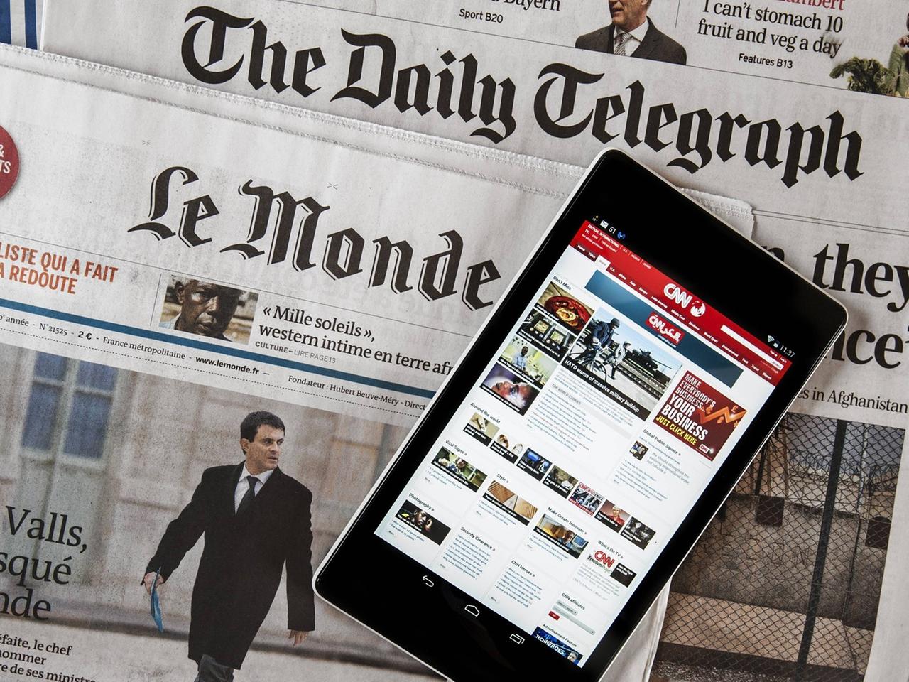 Das Touchscreen eines digitalen Tablets zeigt die CNN International online Nachrichten, welches auf den beiden Zeitungen, der britische "The daily Telegraph" und der französischen "Le monde" liegt. 