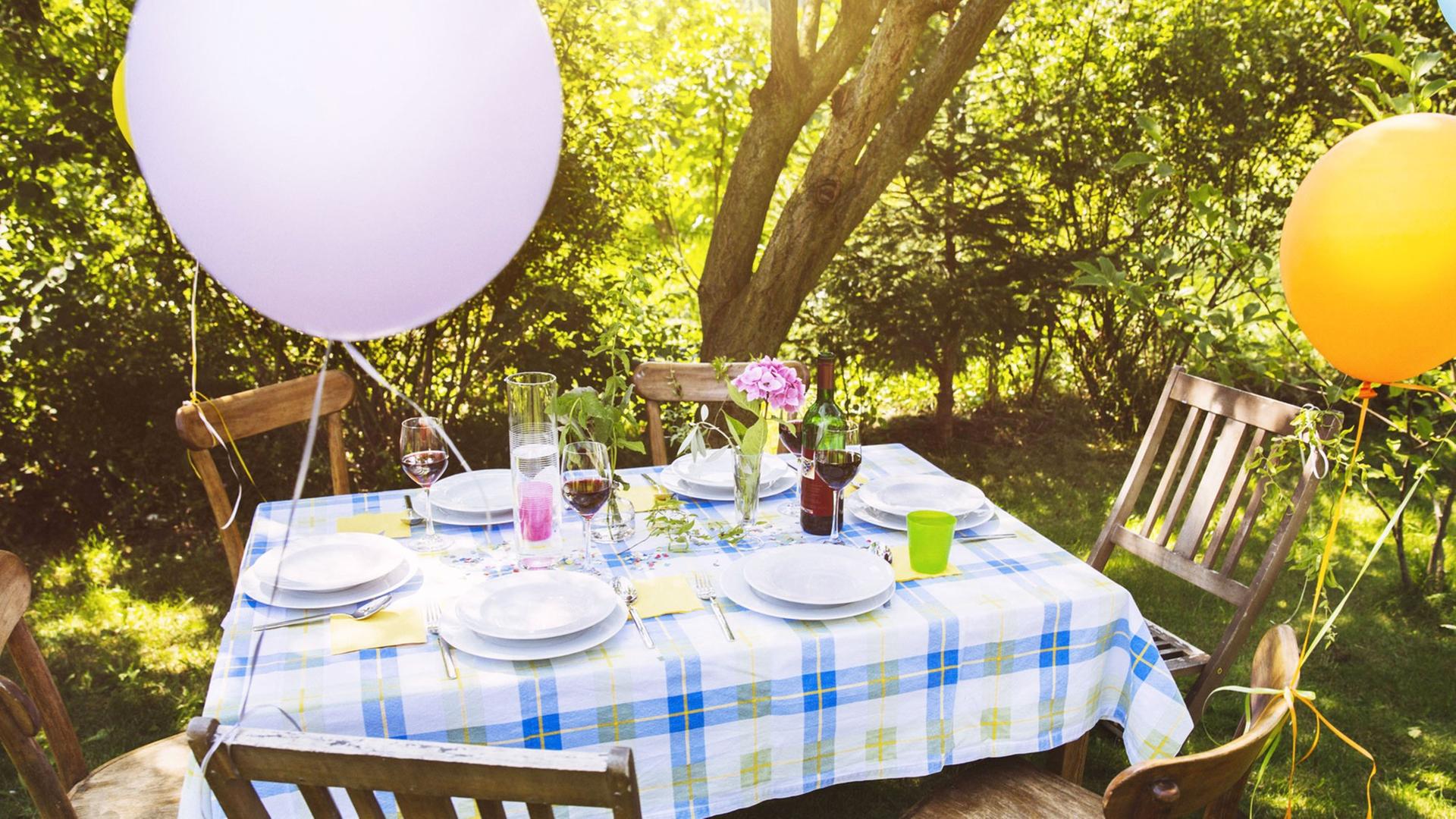 Ein Tisch in einem Garten, an den Stühlen hängen Luftballons. Ein Tisch in einem Garten, an den Stühlen hängen Luftballons.