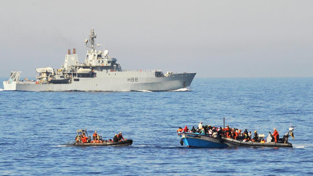 Flüchtlinge werden im Mittelmeer von Bundeswehrsoldaten auf zwei Speedbooten von ihrem Holzboot abgeholt und anschließend zur Fregatte Schleswig-Holstein gebracht. Im Hintergrund ist die britische HMS Enterprise zu sehen. Flüchtlinge werden im Mittelmeer von Bundeswehrsoldaten auf zwei Speedbooten von ihrem Holzboot abgeholt und anschließend zur Fregatte Schleswig-Holstein gebracht. Im Hintergrund ist die britische HMS Enterprise zu sehen.