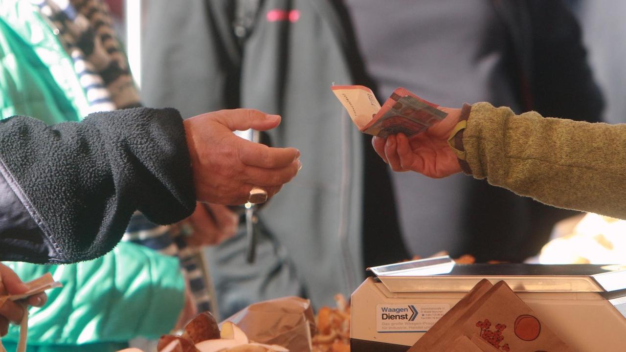 Frau reicht einer Marktverkäuferin Euro-Geldscheine zum Bezahlen ihrer gekaufter Ware. Frau reicht einer Marktverkäuferin Euro-Geldscheine zum Bezahlen ihrer gekaufter Ware.