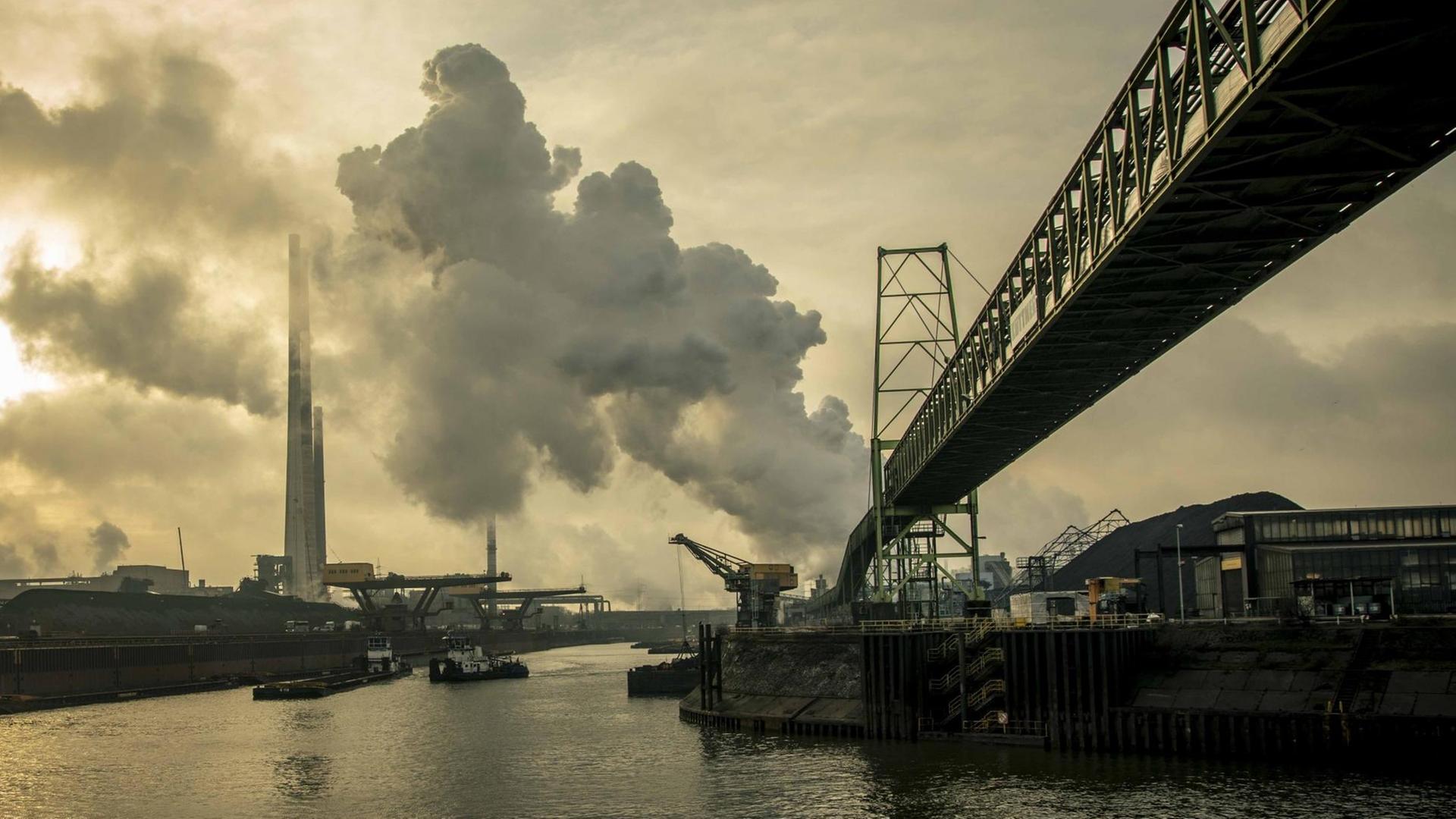 Eine graue Industrielandschaft am Rhein. An den Ufern des Flusses stehen Stahlwerke der Firma Thyssenkrupp. Aus Fabrikschloten steigt Rauch in den Himmel. Eine graue Industrielandschaft am Rhein. An den Ufern des Flusses stehen Stahlwerke der Firma Thyssenkrupp. Aus Fabrikschloten steigt Rauch in den Himmel.