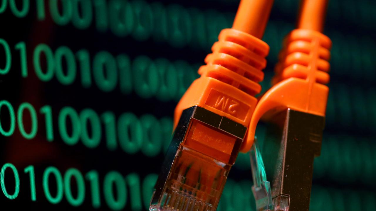 Zwei orangefarbene Netzwerkkabel hängen vor vor einem Computer-Bildschirm, der Zahlenkolonnen mit einem binären Code zeigt. Zwei orangefarbene Netzwerkkabel hängen vor vor einem Computer-Bildschirm, der Zahlenkolonnen mit einem binären Code zeigt.