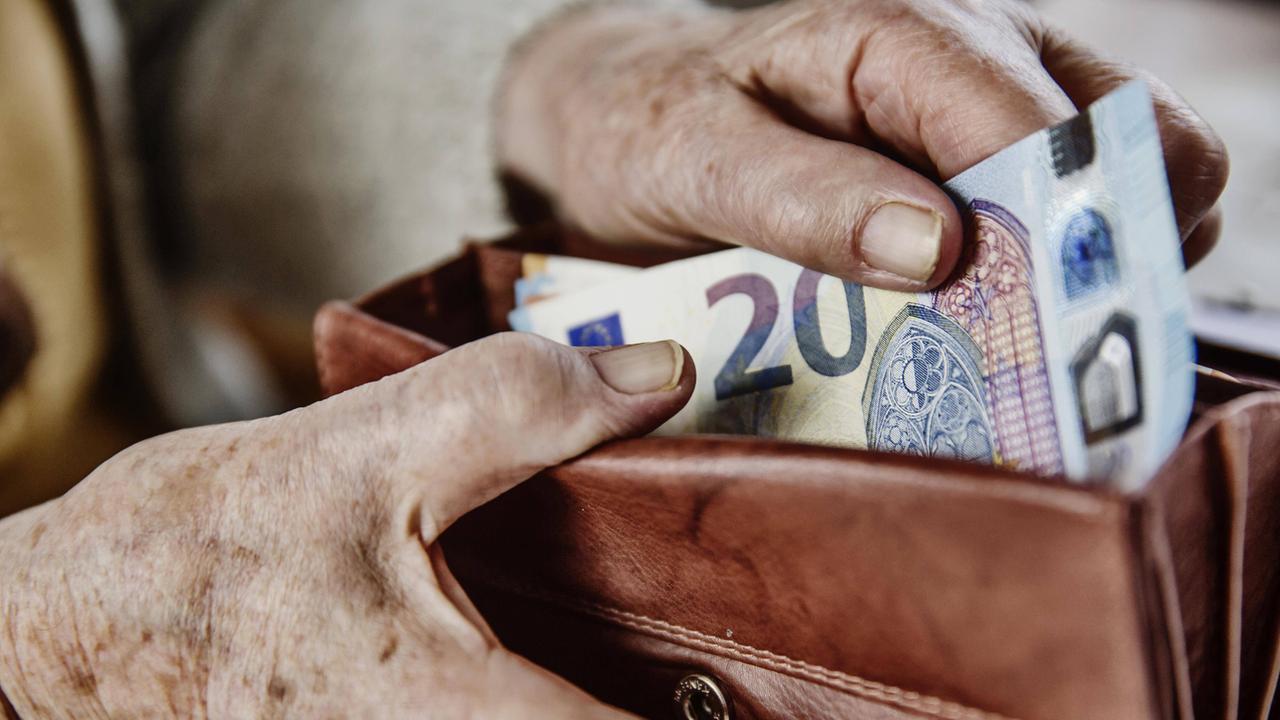 An elderly woman pulls a 20 euro bill out of her wallet.