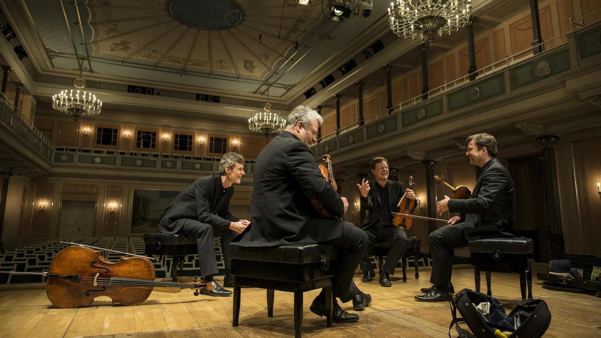 Die vier Musiker sitzen in einer Probensituation auf der Bühne, im Hintergrund der historische "Kleine Saal".