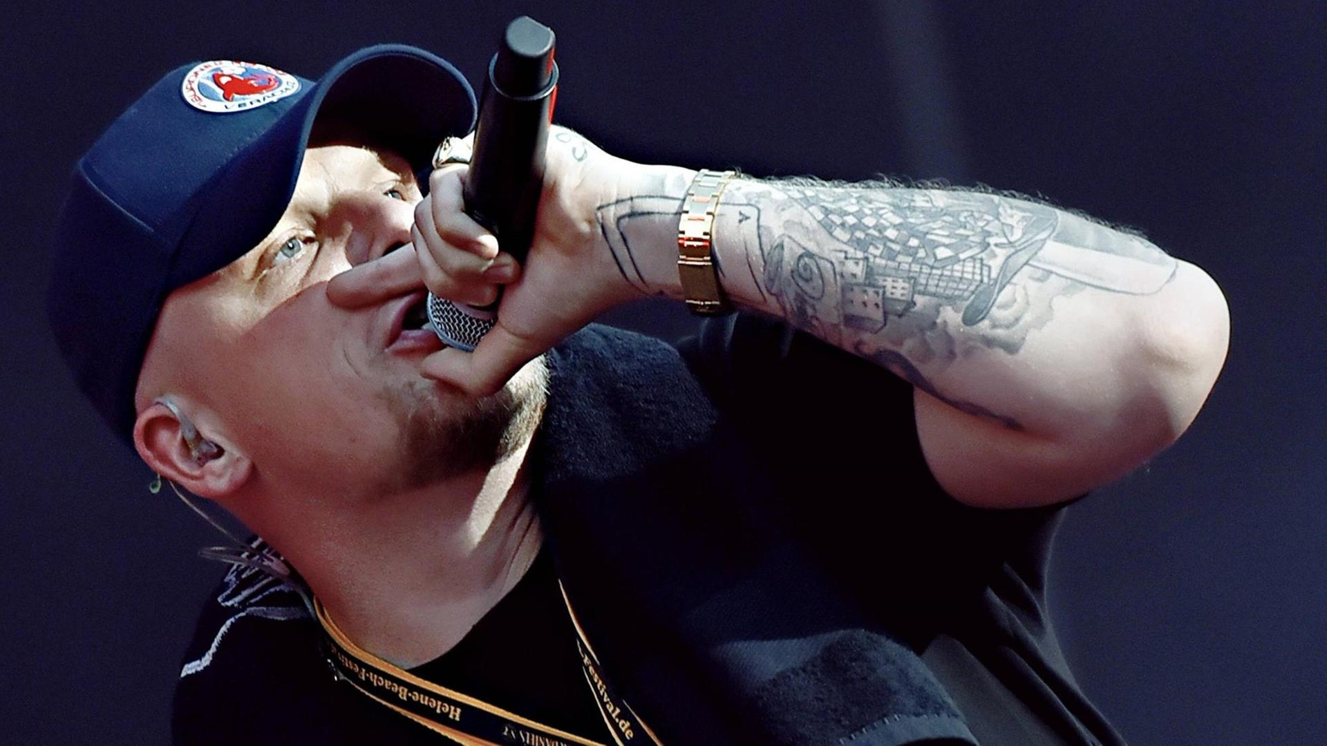 Der Hamburger Rapper Bonez MC steht auf einer Bühne und singt, er hält in der linken Hand ein Mikrofon.
