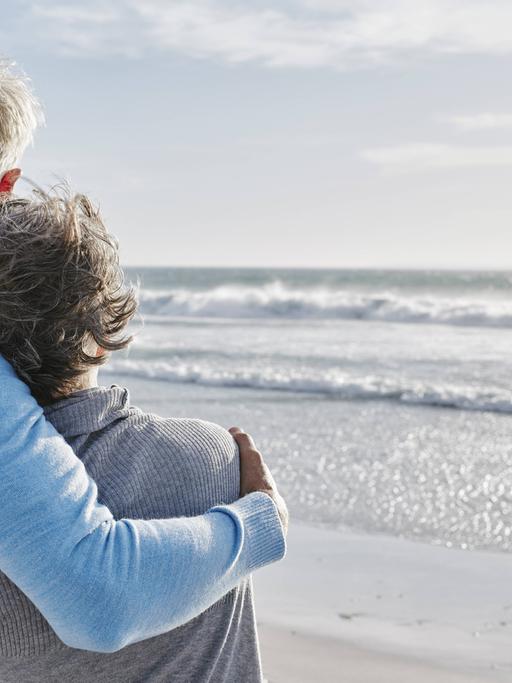 Ein älteres Paar umarmt sich am Strand.