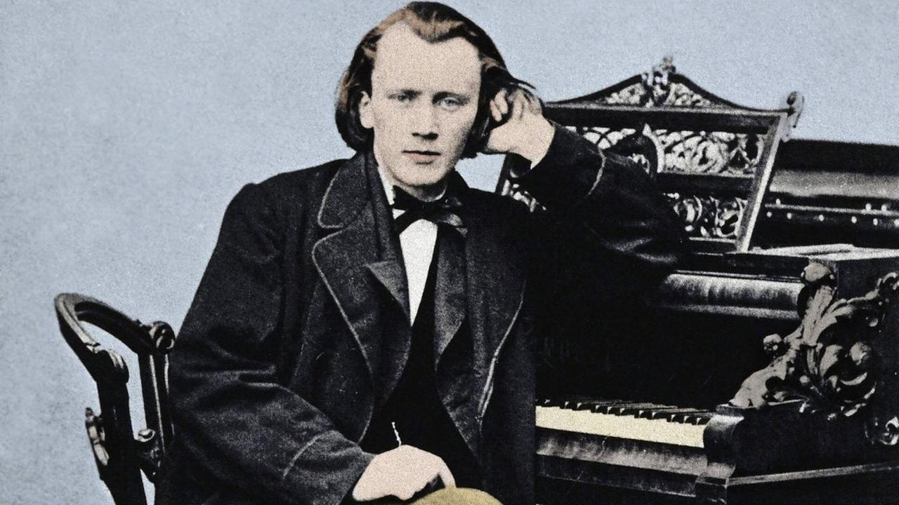 Koloriertes Portrait des jungen Johannes Brahms (1833-1897), sitzend am Klavier, sich mit dem linken Arm aufstützend.