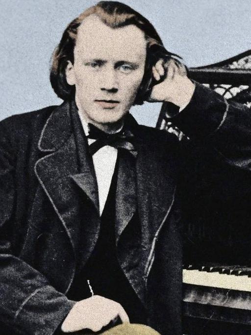 Koloriertes Portrait des jungen Johannes Brahms (1833-1897), sitzend am Klavier, sich mit dem linken Arm aufstützend.
