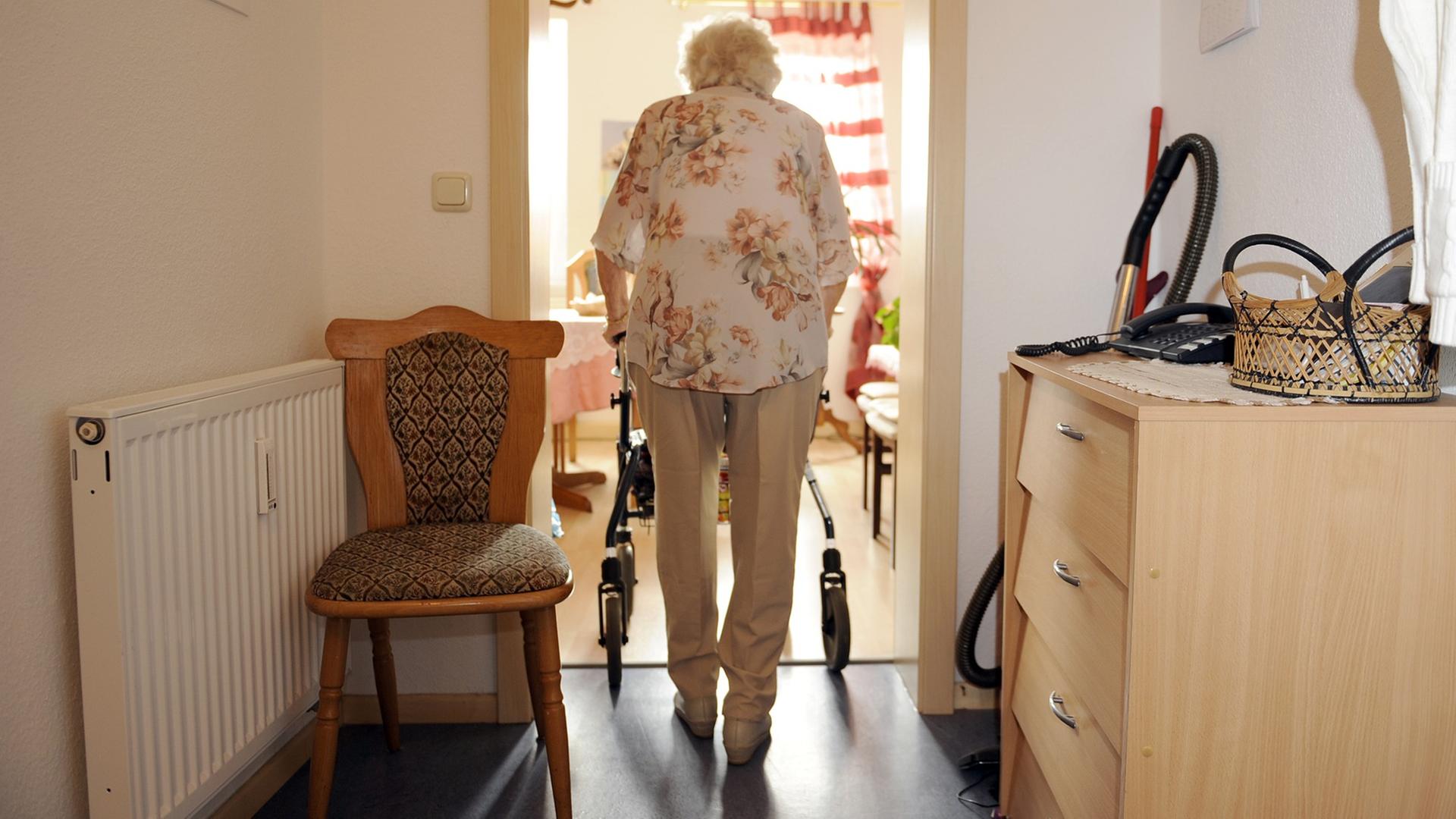 Eine ältere Frau geht am Rollator vom Wohnungsflur in ein Zimmer. Eine ältere Frau geht am Rollator vom Wohnungsflur in ein Zimmer.