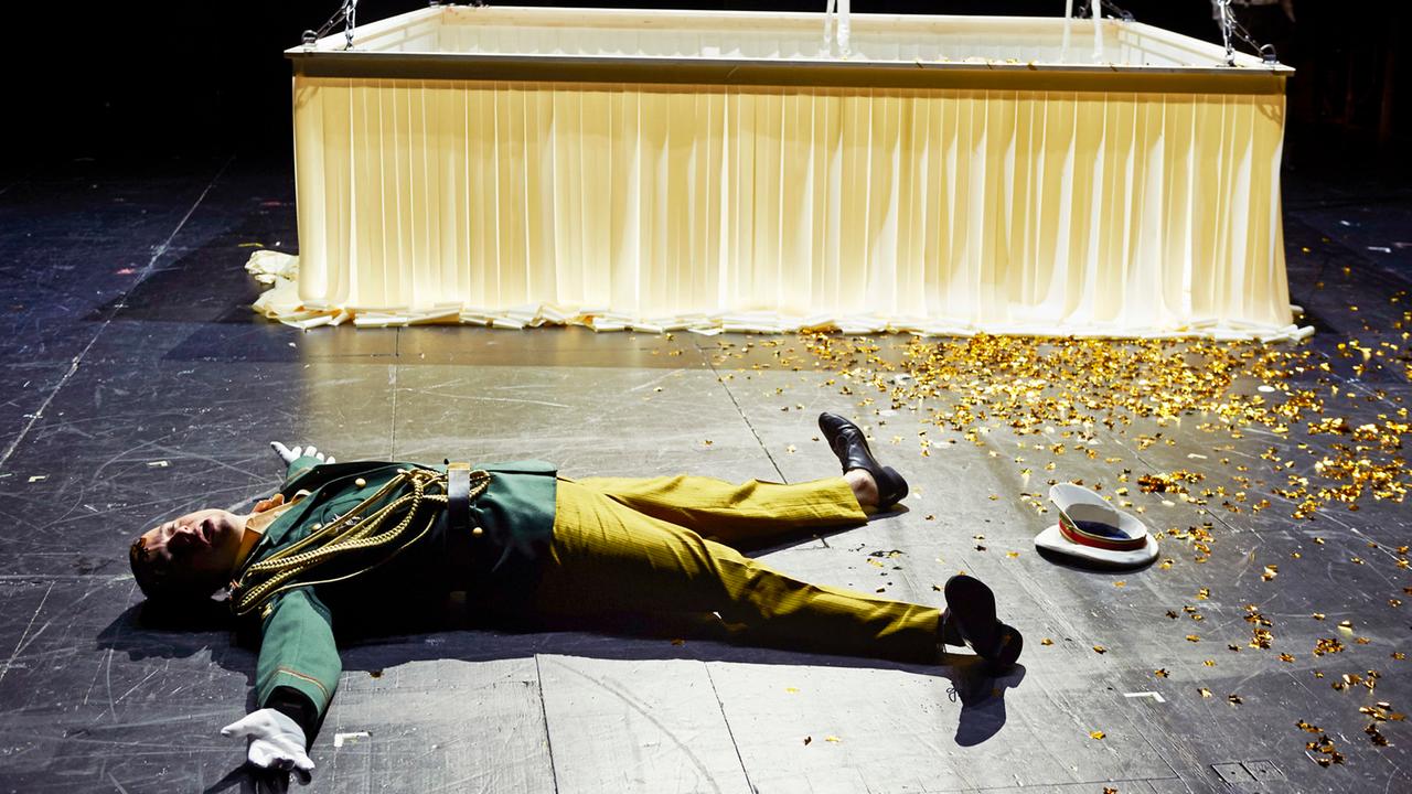 Das Bild zeigt eine liegende Person auf einer Theaterbühne. Das Bild zeigt eine liegende Person auf einer Theaterbühne.