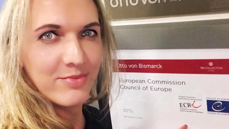 Julia Monro blickt in die Kamera und zeigt mit dem Finger hinter sich auf ein Schild. Julia Monro blickt in die Kamera und zeigt mit dem Finger hinter sich auf ein Schild.