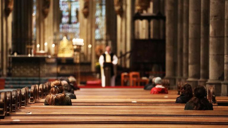 Gläubige sitzen während eines Gottesdienstes in den Sitzreihen im Kölner.
