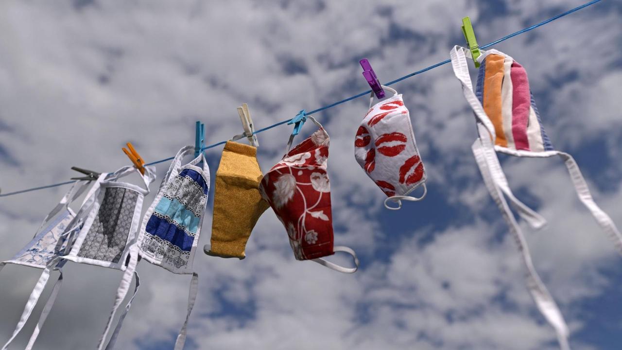 Auf einer Wäschleine hängen bei gutem Wetter verschiedene Stoffmasken mit bunten Motiven. Auf einer Wäschleine hängen bei gutem Wetter verschiedene Stoffmasken mit bunten Motiven.