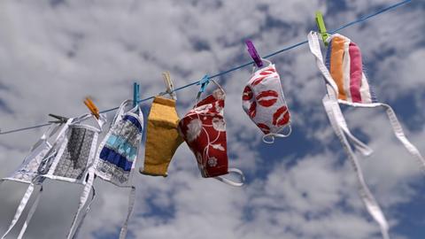 Auf einer Wäschleine hängen bei gutem Wetter verschiedene Stoffmasken mit bunten Motiven.
