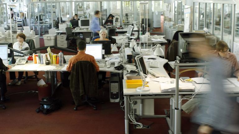 Menschen sitzen an ihren Arbeitsplätzen in einem Großraumbüro.