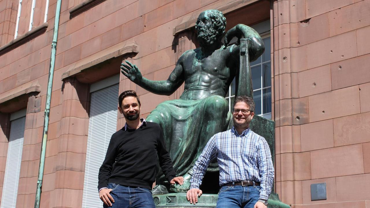 Kirchenhistoriker Thomas Jürgasch (links) und der Religionspädagoge Johannes Heger (rechts) stehen vor Homer Simpsons Namensvetter "Homer"